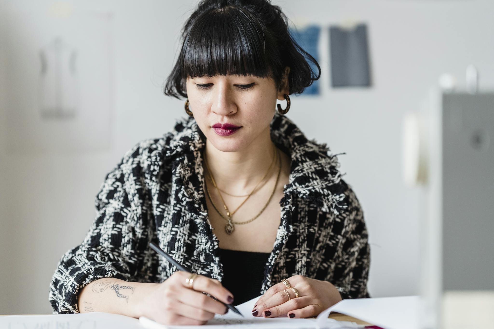 Asian female drawing on paper while working on clothing design on blurred background